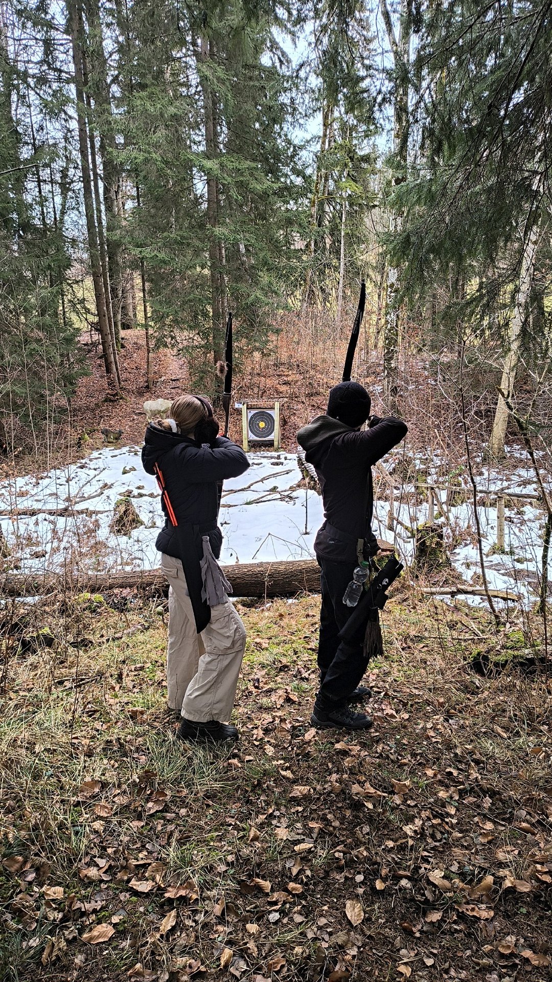 Zwei Kinder zielen mit Bögen auf eine Zielscheibe im Wald